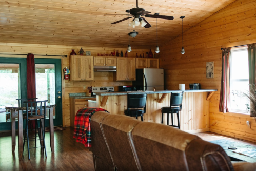 Cozy wooden cabin interior with a kitchen, dining area, and living space featuring a sofa and rustic decor.