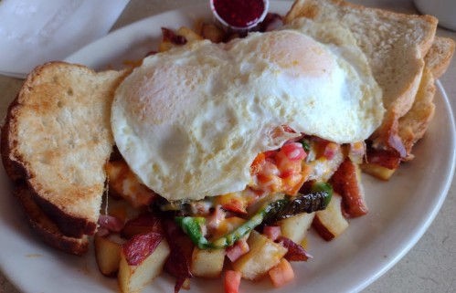 A plate of breakfast featuring two fried eggs on a bed of potatoes, cheese, and vegetables, with toast on the side.