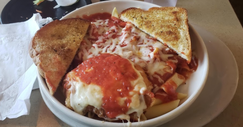 A bowl of pasta topped with marinara sauce, melted cheese, and two slices of toasted bread on the side.