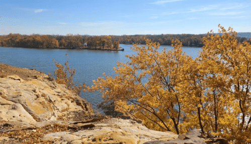 A scenic view of a river surrounded by autumn trees and rocky terrain under a clear blue sky.