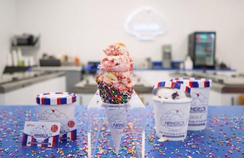 A colorful ice cream cone topped with sprinkles, surrounded by ice cream tubs on a vibrant blue table.