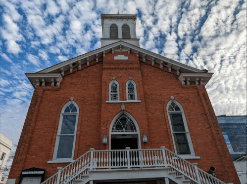 A red brick church with a white staircase, under a sky filled with fluffy clouds.