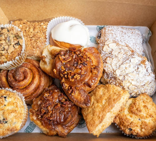 A variety of baked goods in a box, including pastries, scones, and cinnamon rolls, arranged neatly with paper liners.