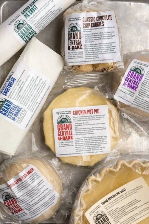 Assorted packaged baked goods, including cookies, pie shells, and a chicken pot pie, on a silver tray.