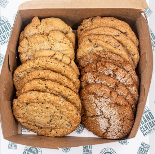 A box filled with assorted cookies, including chocolate chip and sugar cookies, on a branded background.