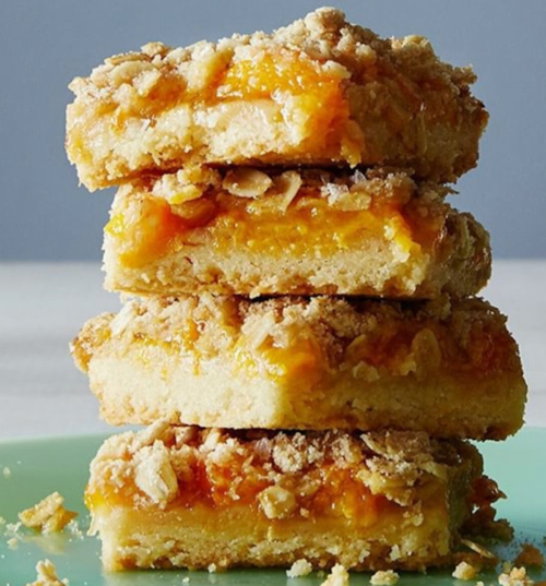 A stack of four golden peach crumble bars on a green plate, showcasing a crumbly topping and vibrant filling.
