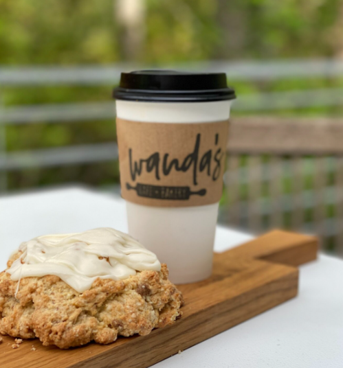 A coffee cup with a brown sleeve next to a large cookie on a wooden board, set against a blurred green background.