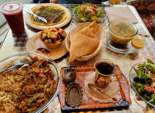 A table spread with various dishes: rice, salad, soup, fruit, pastries, and tea, all on a decorative tablecloth.