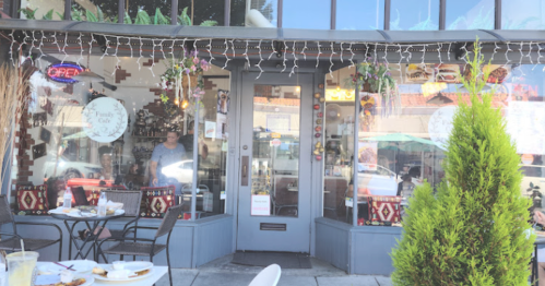 A cozy restaurant with outdoor seating, decorated with lights and plants, and a welcoming open sign in the window.