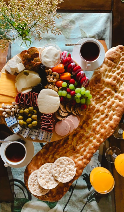 A colorful charcuterie board with fruits, cheeses, meats, and snacks, accompanied by coffee and orange juice.