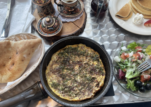 A table setting with a skillet of herb omelette, bread, salad, coffee, and pancakes on a decorative wooden tray.
