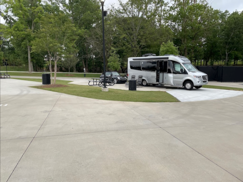 A white RV parked in a grassy area with picnic tables and trees in the background.