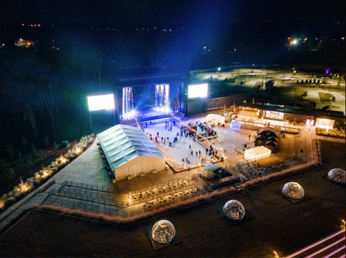 Aerial view of a nighttime outdoor amphitheater with a stage, tents, and illuminated pathways.