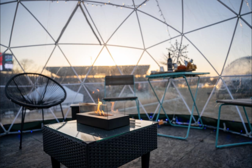 Cozy dome interior with a fire pit, chairs, and a view of a sunset outside.