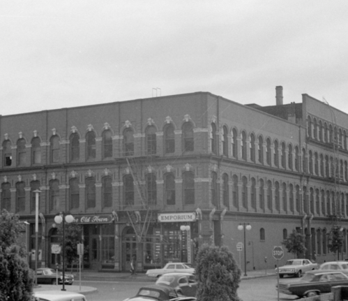 Historic brick building with arched windows, featuring a storefront labeled "Old Tower Emporium" and parked cars in front.
