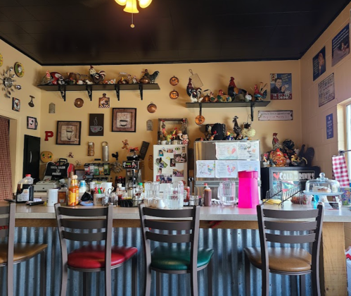 A cozy diner interior with a counter, colorful decor, and shelves filled with knick-knacks and memorabilia.