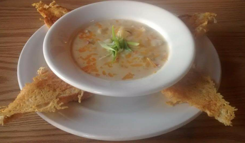 A bowl of creamy soup topped with green onions, surrounded by crispy fried bread triangles on a white plate.