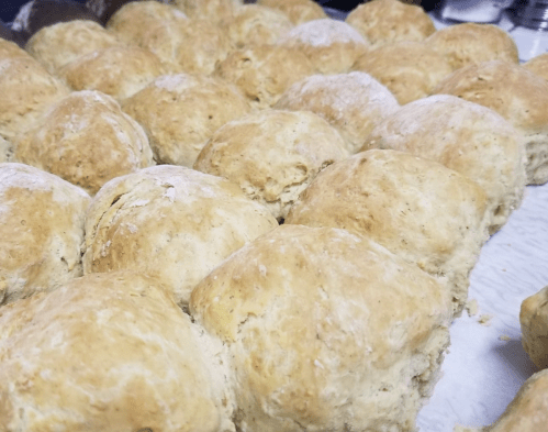 Freshly baked, golden-brown biscuits arranged closely on a baking sheet.