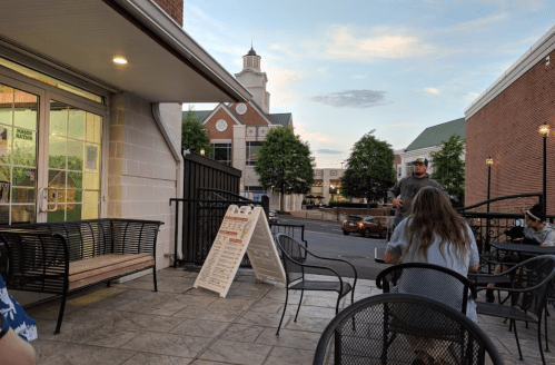 Outdoor seating area at a café with people chatting, a sign, and a view of a building in the background.