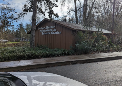 Sign for Delbert Hunter Arboretum and Botanic Garden, surrounded by trees and greenery on a cloudy day.