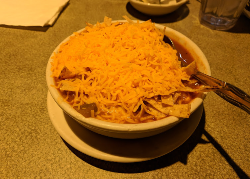 A bowl of chili topped with shredded cheese and tortilla strips, served on a plate.