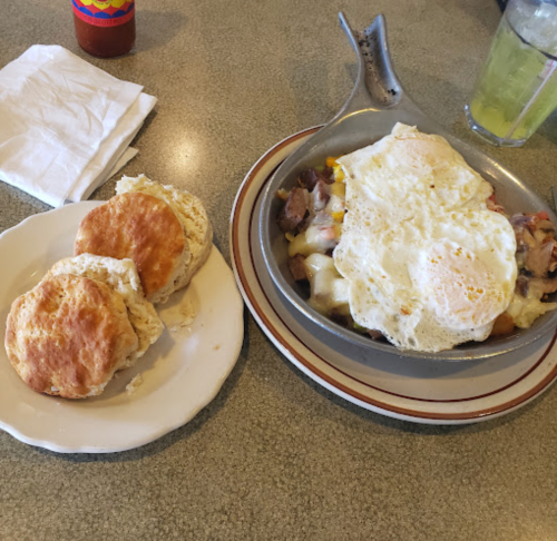 A plate with two biscuits and a bowl of breakfast hash topped with fried eggs.