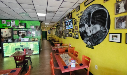 A vibrant restaurant interior with yellow walls, colorful tables, and a mural of a couple on one wall.