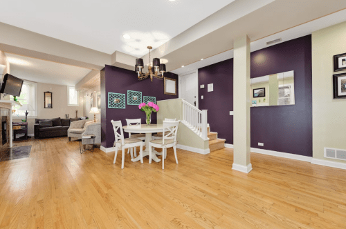 Bright, modern living space with a dining table, purple accent wall, and staircase leading to an upper level.