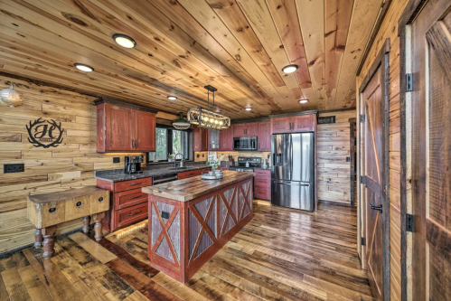 Cozy rustic kitchen with wooden walls, red cabinets, and a large island, featuring modern appliances and warm lighting.