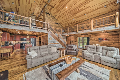 Cozy wooden cabin interior with a spacious living area, plush sofas, and a lofted balcony overlooking the kitchen.