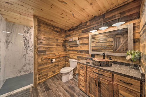 A rustic bathroom featuring wooden walls, a stone sink, and a modern shower with marble accents.