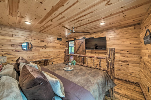 Cozy bedroom with wooden walls, a rustic bed, and a mounted TV, featuring warm lighting and a natural decor style.