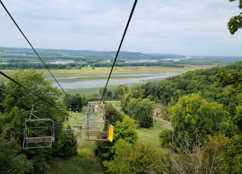 A scenic view from a chairlift overlooking lush green hills and a winding river below.