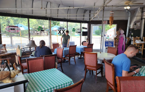 A cozy restaurant interior with tables, chairs, and patrons, featuring a green checkered tablecloth and large windows.