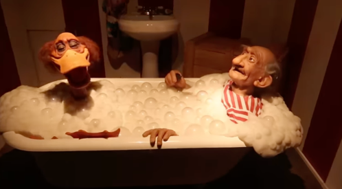 Two animated characters, a duck and an elderly man, relax in a bubble-filled bathtub in a whimsical setting.