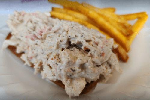 A plate featuring a generous serving of creamy chicken salad on a bun, accompanied by golden French fries.