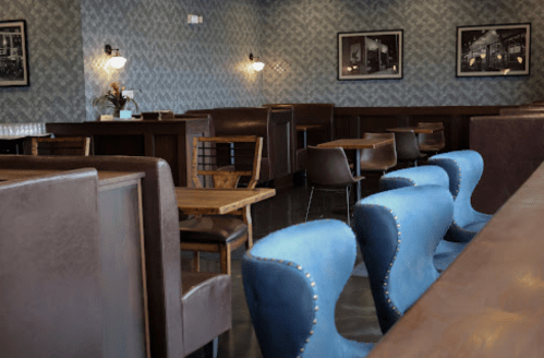 Cozy café interior with blue chairs, wooden tables, and patterned walls adorned with black-and-white photos.