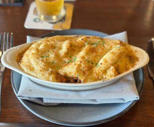 A creamy, golden-brown shepherd's pie served in a white dish on a blue plate, garnished with parsley.