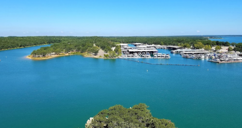 Aerial view of a serene lake with marinas, surrounded by lush greenery and clear blue skies.
