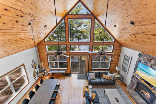 Cozy cabin interior with wooden walls, large windows, and a view of the lake, featuring a dining table and comfortable seating.