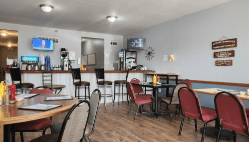 Cozy restaurant interior with wooden tables, red chairs, a bar area, and a coffee station in the background.