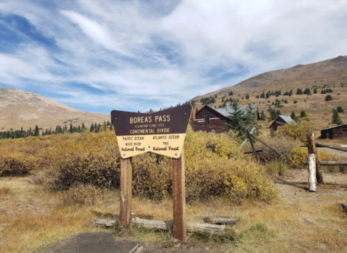 Sign for Boreas Pass, indicating the Continental Divide, with mountains and autumn foliage in the background.