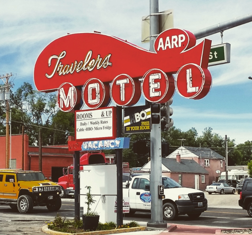 Bright red vintage sign for Travelers Motel, featuring AARP, with details on rates and amenities.