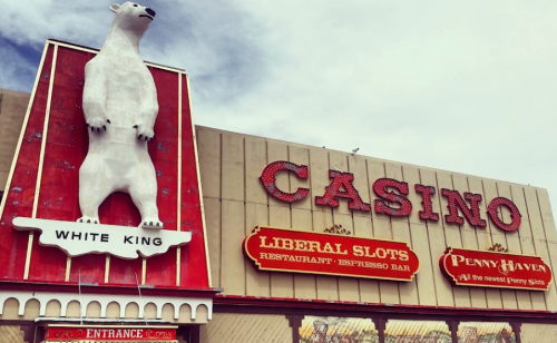 Signage of a casino featuring a large polar bear statue and text for various attractions, under a cloudy sky.