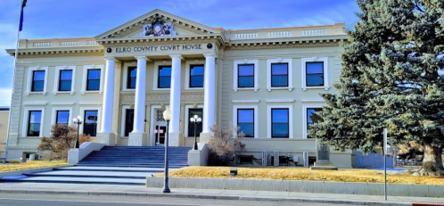 Historic Elko County Courthouse with columns, large windows, and a landscaped front yard under a clear blue sky.
