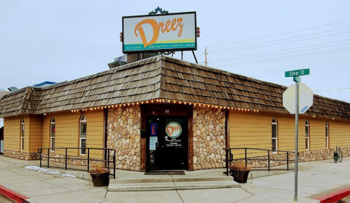 Exterior of a restaurant named "Dreez," featuring a stone and wood facade, with a sign and nearby street corner.