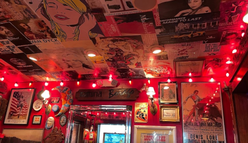 A vibrant room with a ceiling covered in colorful posters and red lights, creating a lively, retro atmosphere.