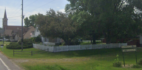 A small town entrance sign reading "Welcome to St. George," with trees and a church in the background.