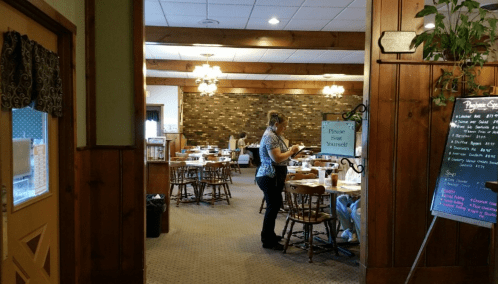 A cozy restaurant interior with wooden decor, tables set for dining, and a server attending to customers.