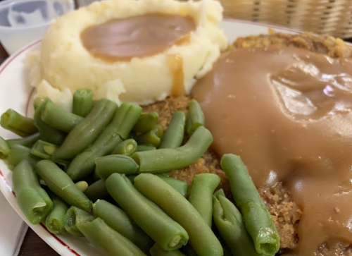 A plate of food featuring fried chicken with gravy, mashed potatoes, and green beans.